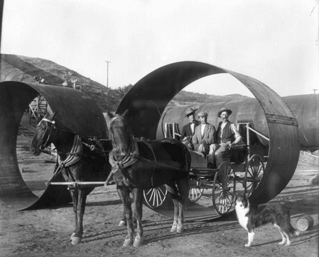 (n.d.)* - To emphasize the size of the Aqueduct pipe, three men on a horse-drawn wagon are positioned within a pipe section. It appears the dog in the photo is also posing for the camera.