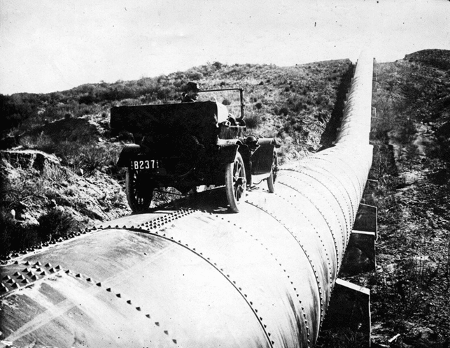 (ca. 1913)*^^ - A man is seen behind the wheel of an early model car sitting on top of a completed section of the LA Aqueduct.