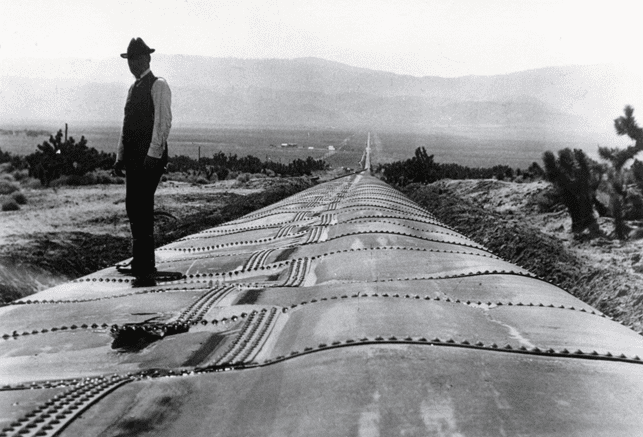 (1914)*^ – View showing William Mulholland standing on a section of the Antelope Siphon damaged by a major flood. Note: Water pressure alone would restore the pipe to its original circular form.