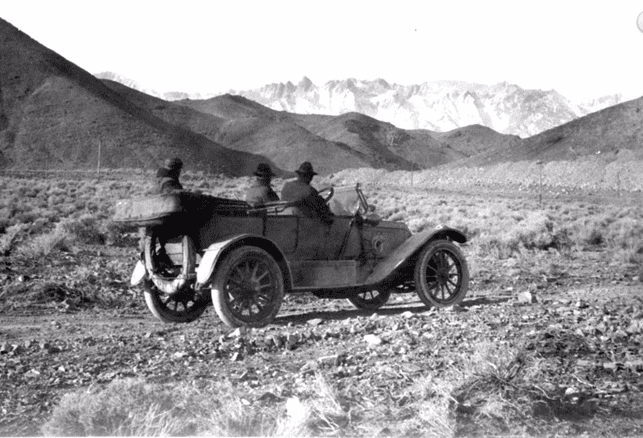 (ca. 1907)^*– View showing William Mulholland along with two others, sitting in a car in the Owens Valley. All three are looking toward the snow covered Eastern Sierras, water source of the yet to be built L.A. Aqueduct.